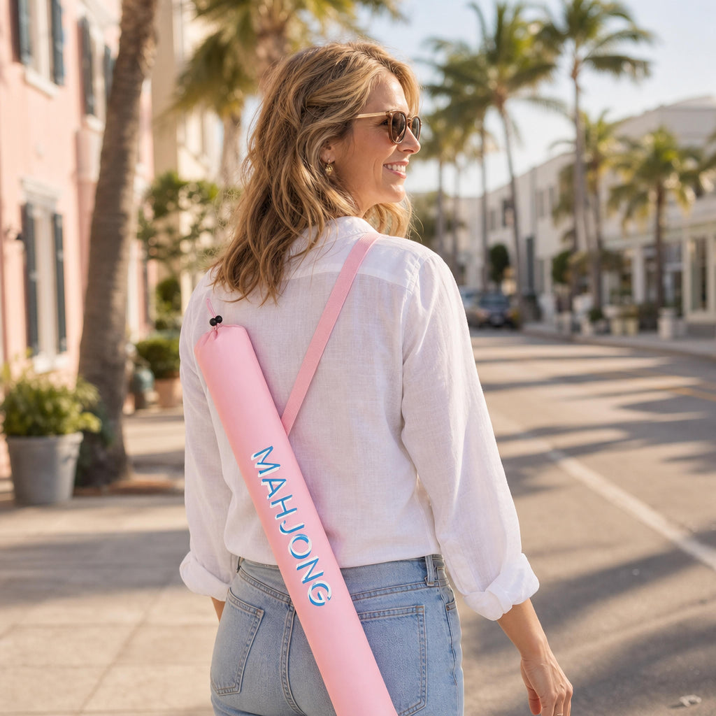Woman carrying a light pink mahjong mat carry bag over her shoulder on a sunny palm-lined street