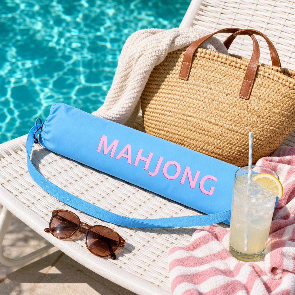 Blue mahjong mat carry bag on a poolside lounge chair with a straw tote and lemonade