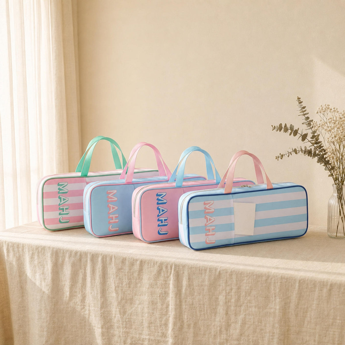 Four pink and blue striped MAHJ mahjong rack bags with top handles lined up on a table